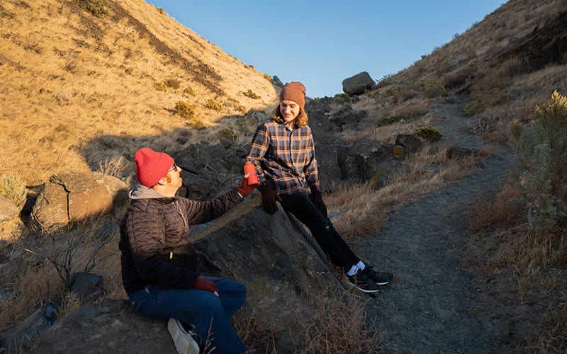 2 men sitting on rocks wearing hats and gloves drinking water